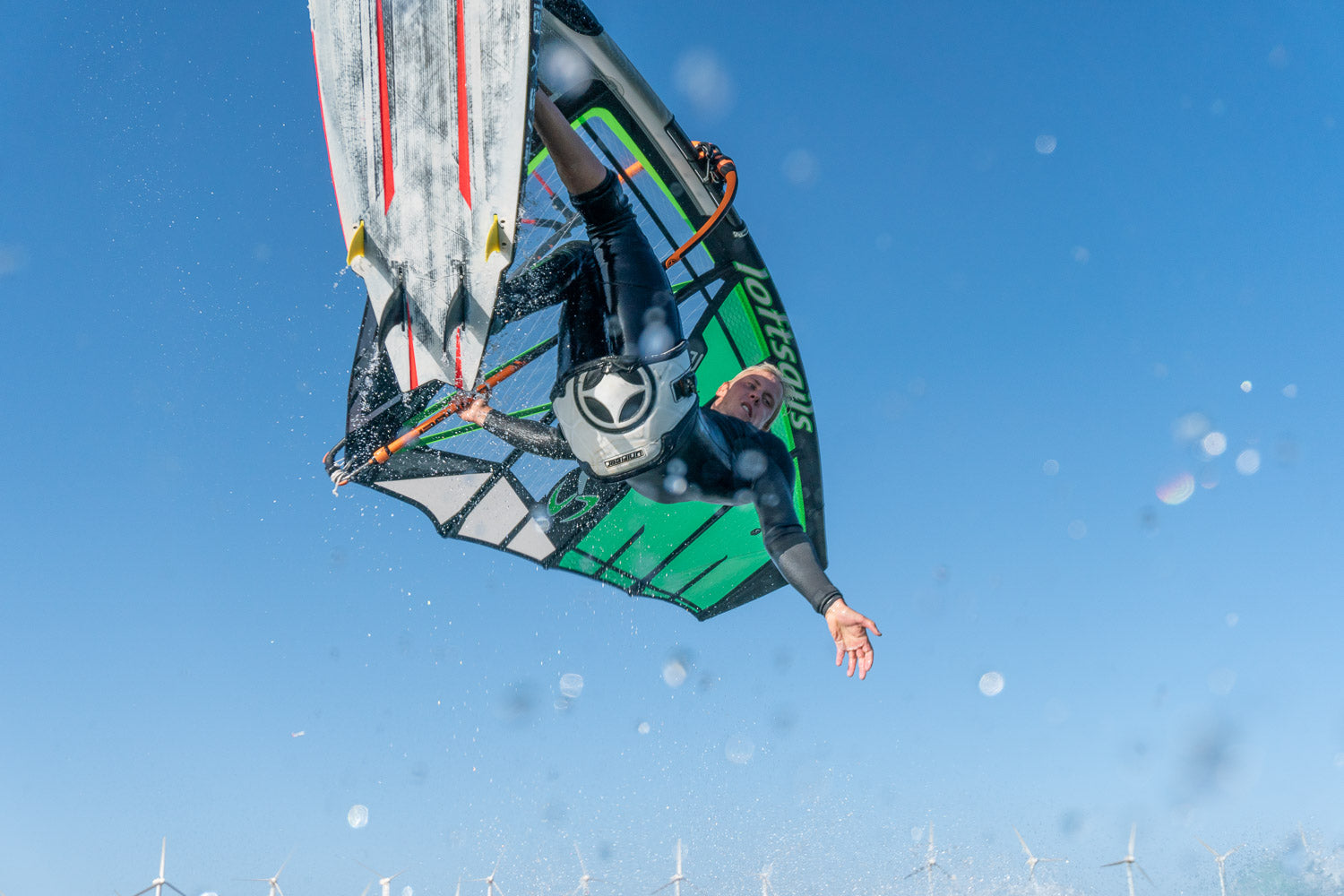 Person windsurfing against a clear blue sky with wind turbines in the background