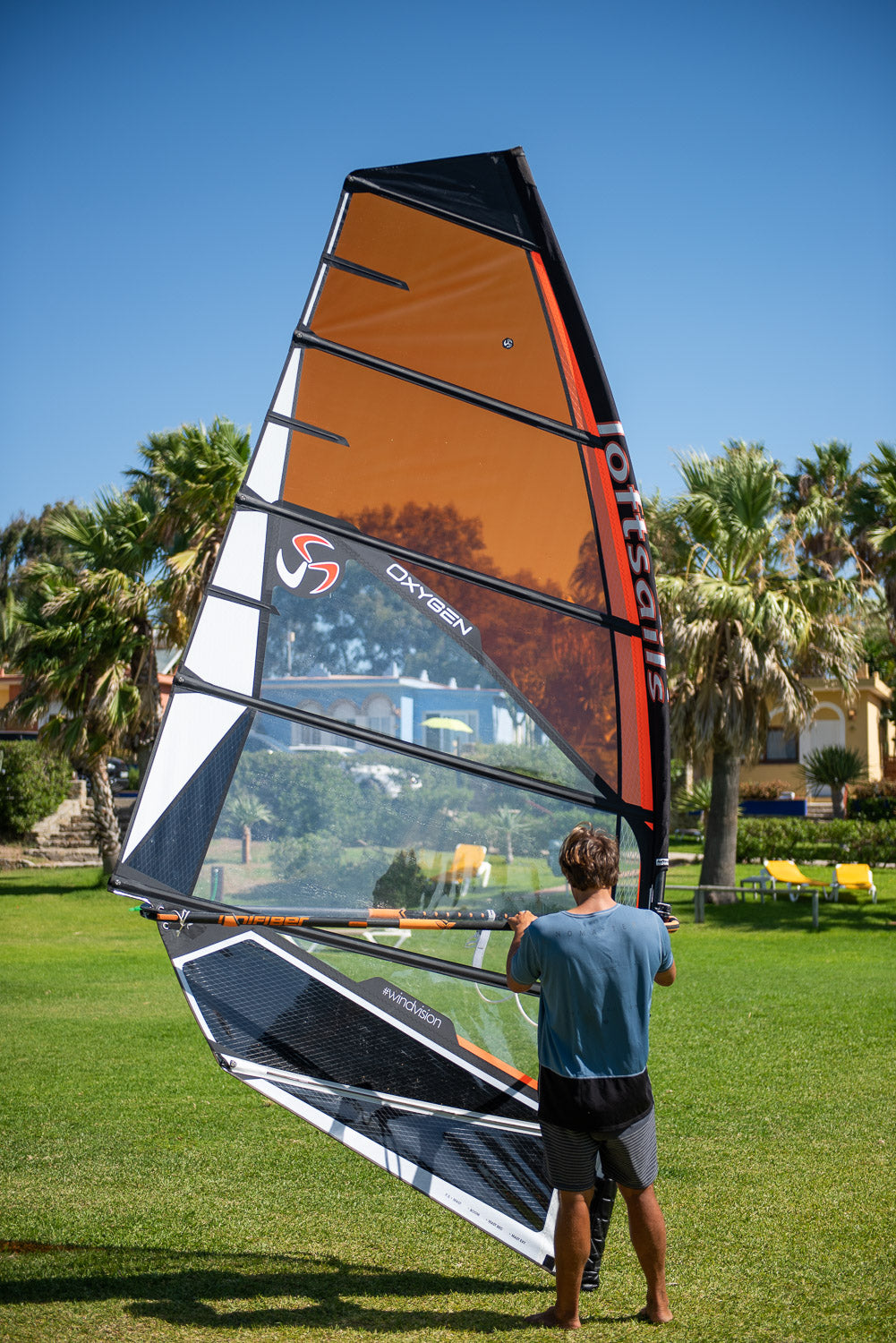 Person holding a large orange and black sail in a park with palm trees in the background