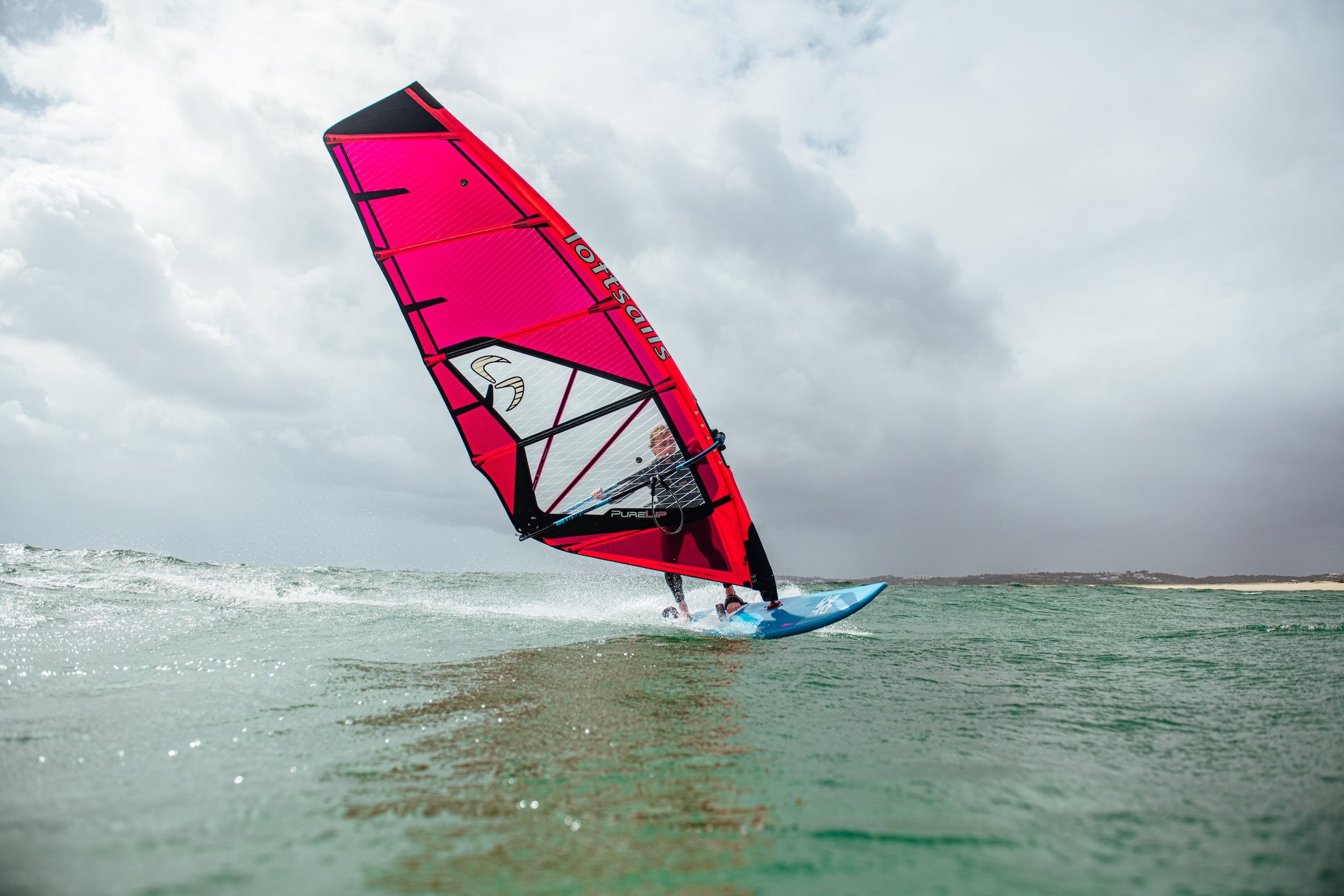 Person windsurfing on a cloudy day with a red sail.
