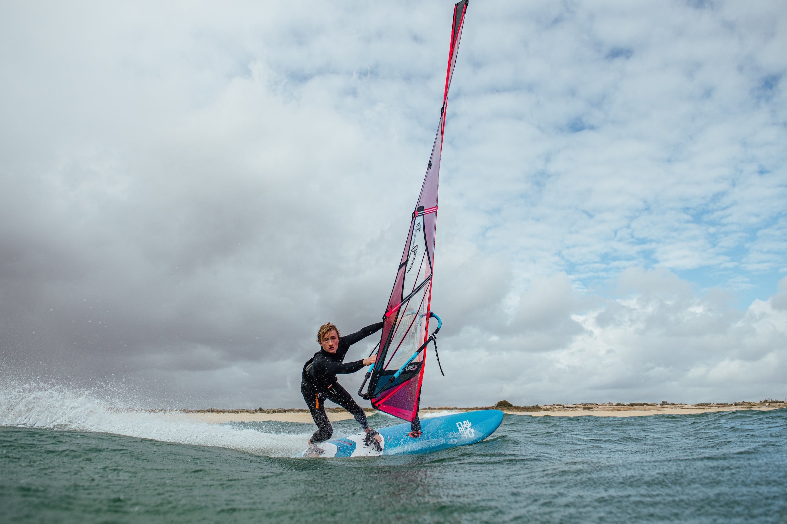 Person windsurfing on a body of water with a cloudy sky.