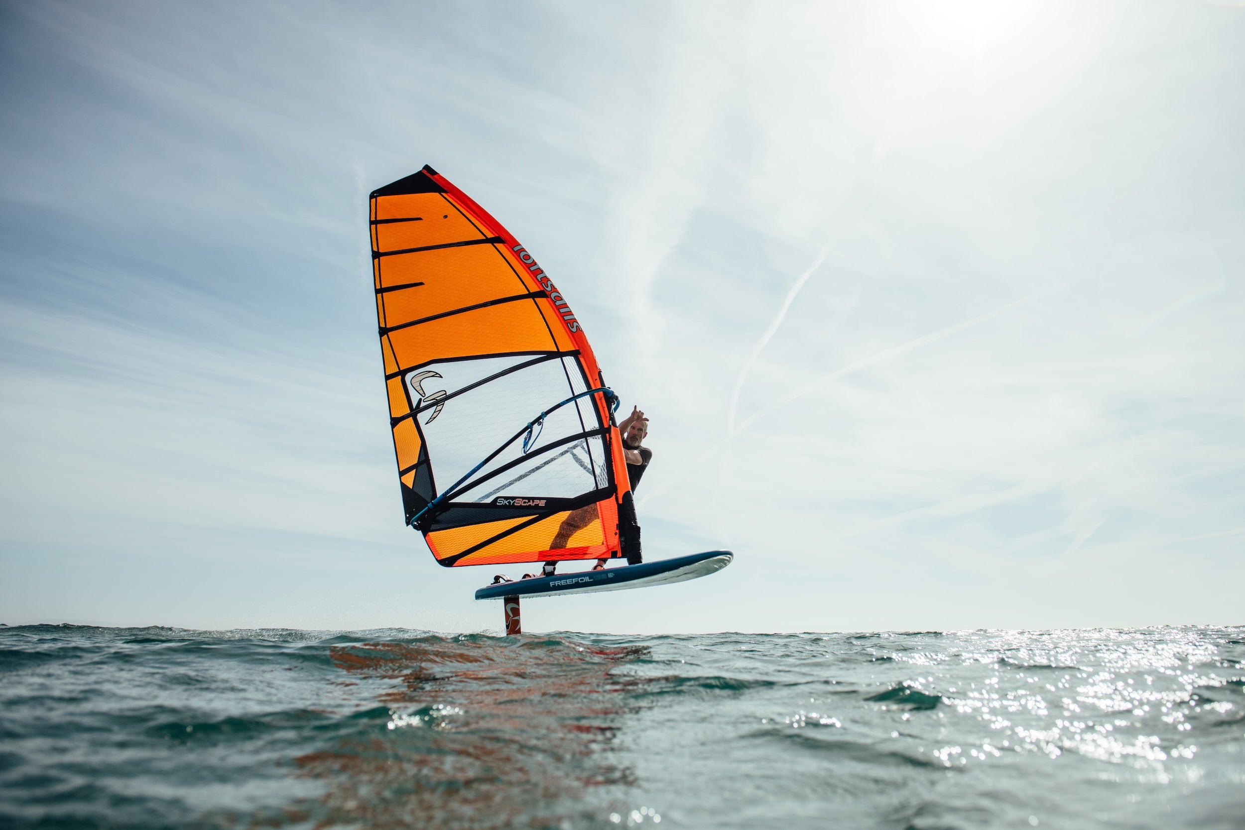 Person windsurfing on a clear day with an orange sail.