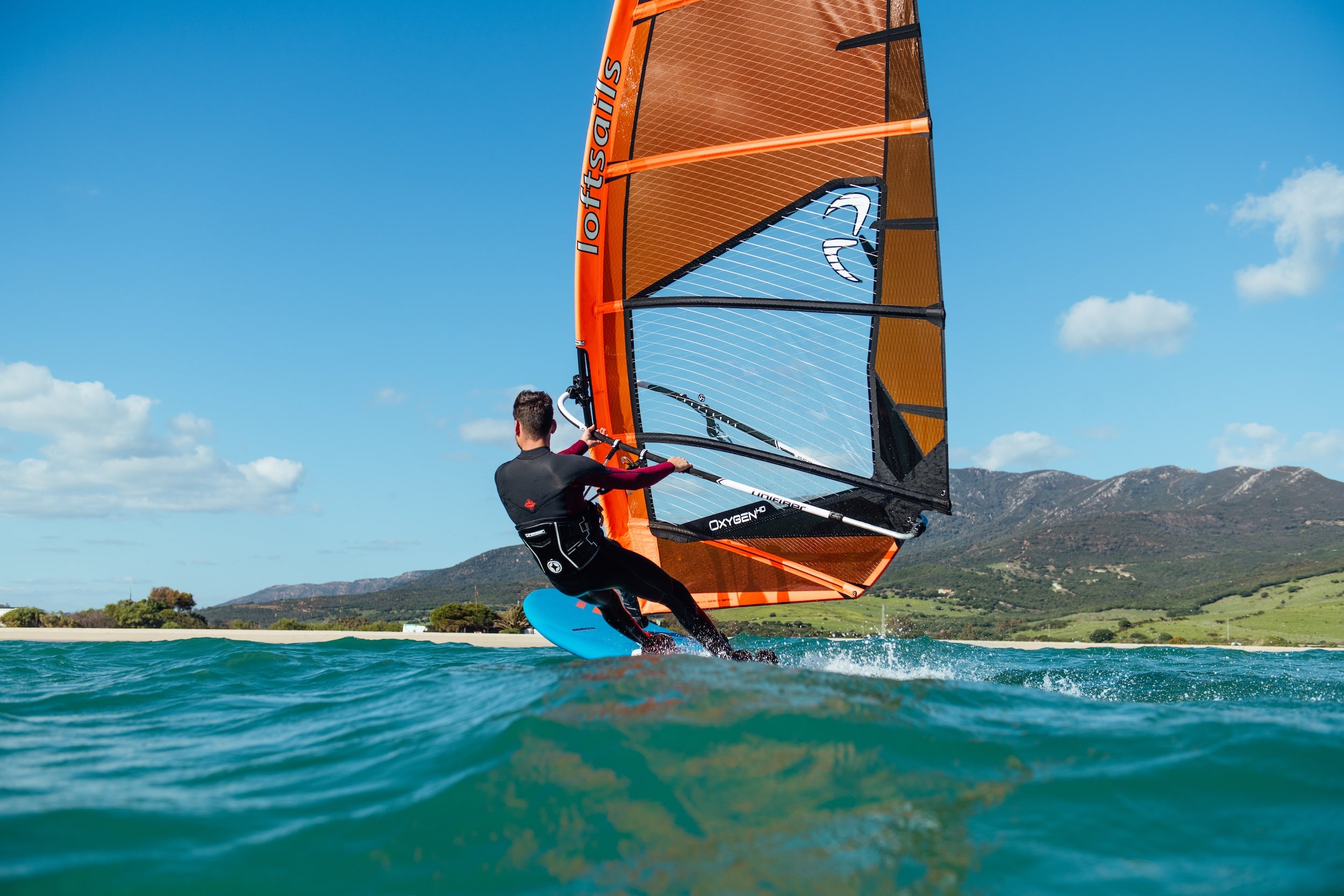 Person windsurfing on a blue ocean with mountains in the background