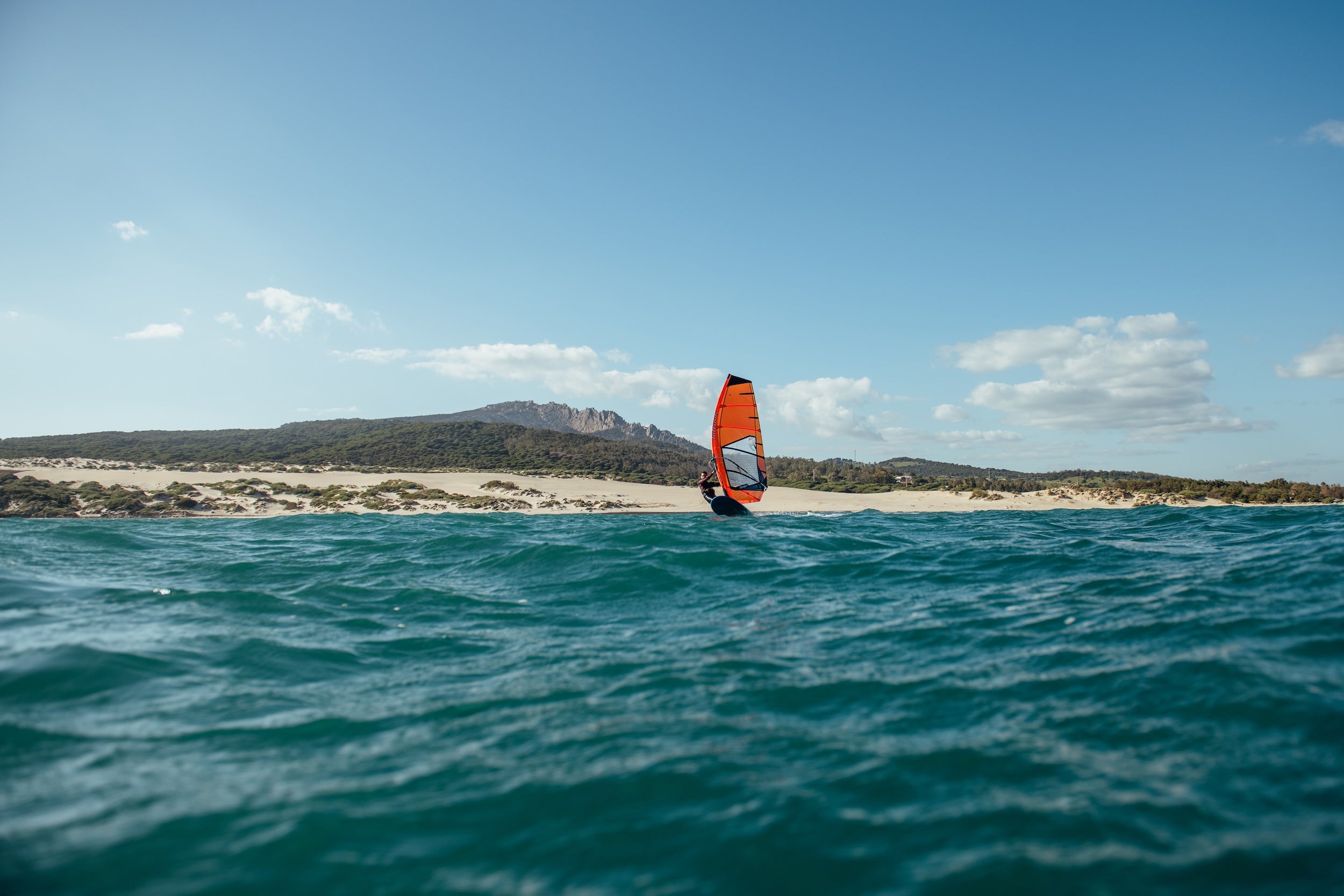 Person windsurfing on a body of water with a clear sky and distant landmass.