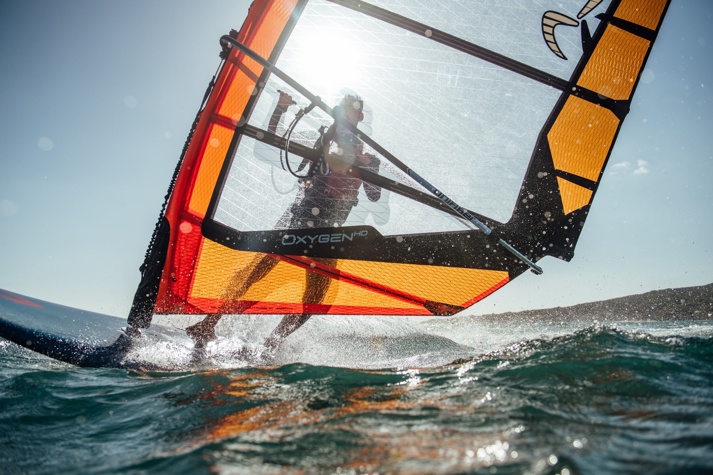 Person windsurfing on a clear day with a colorful sail.