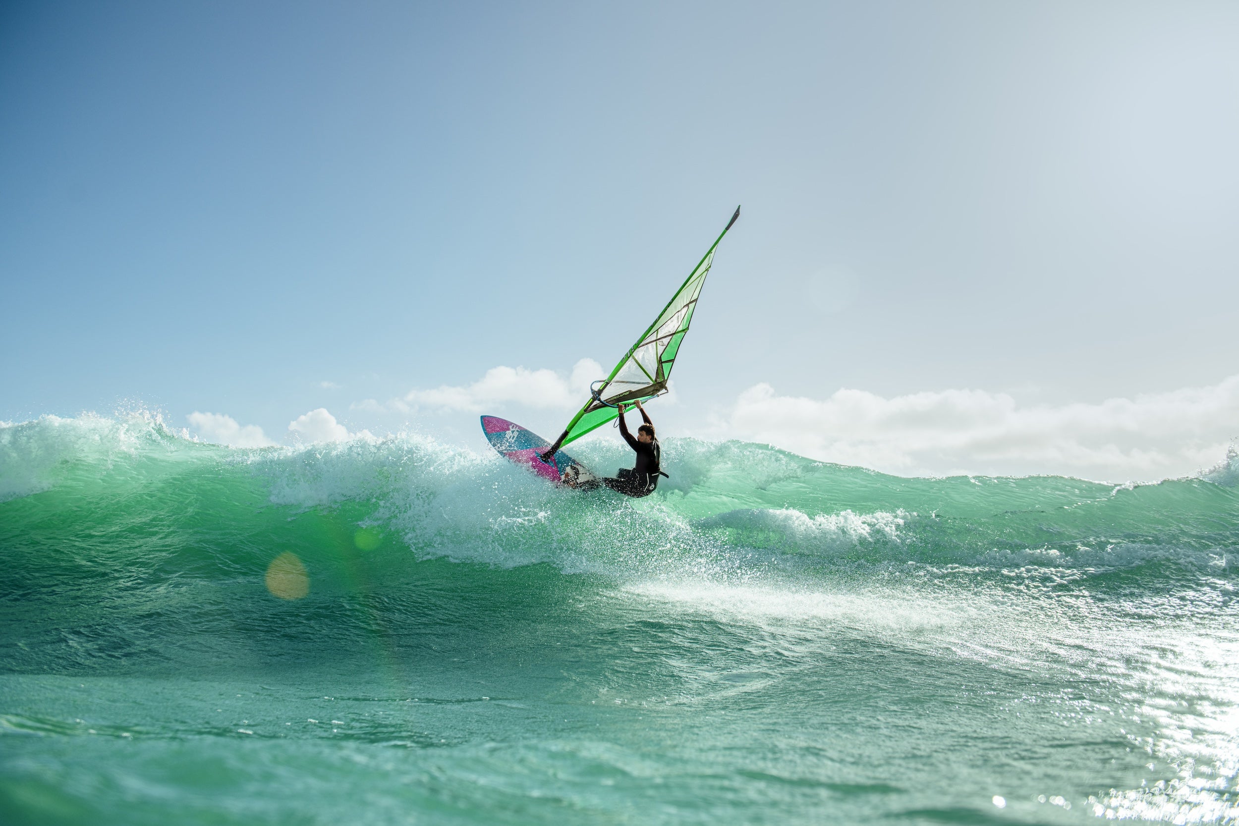 Person windsurfing on a wave with a clear sky