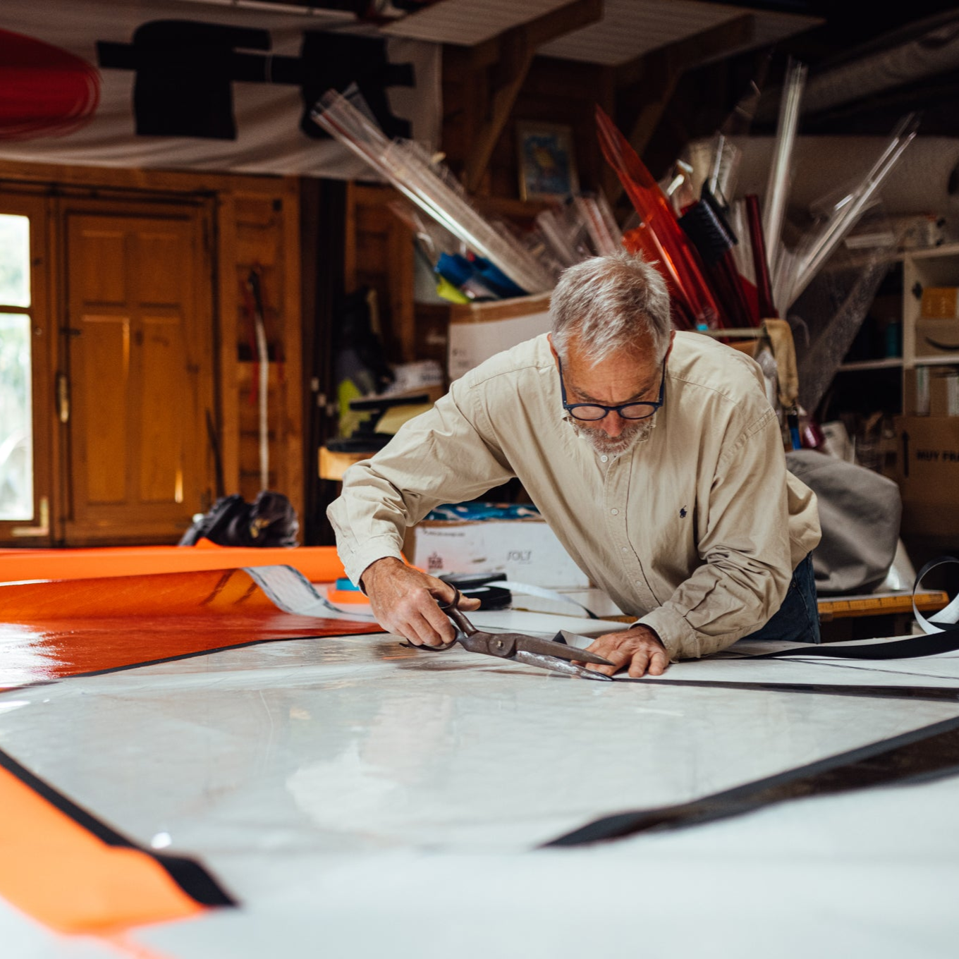 Man working on a windusrf sail in a workshop with various equipment around.