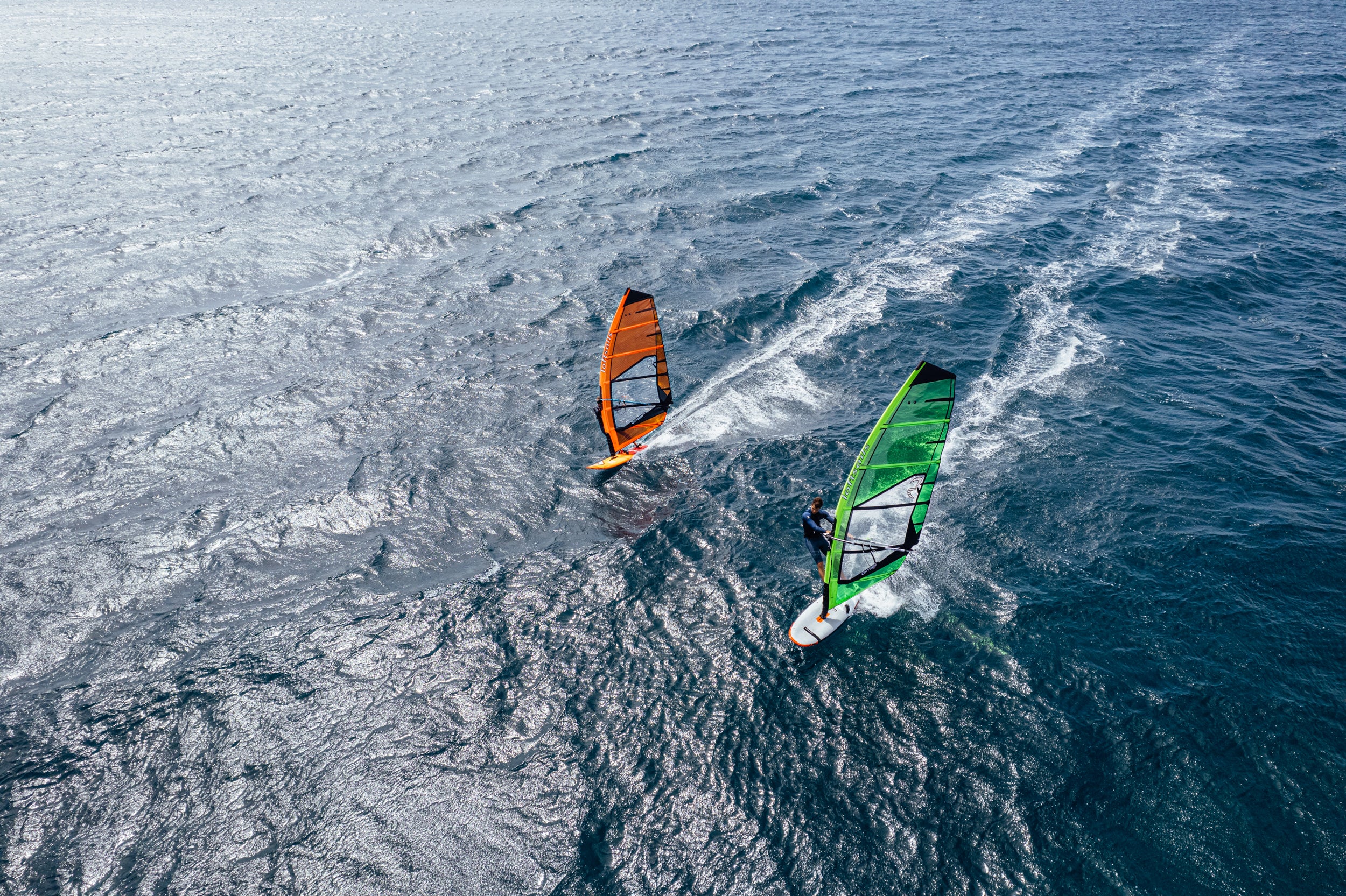 Two windsurfers on the water with colorful sails.