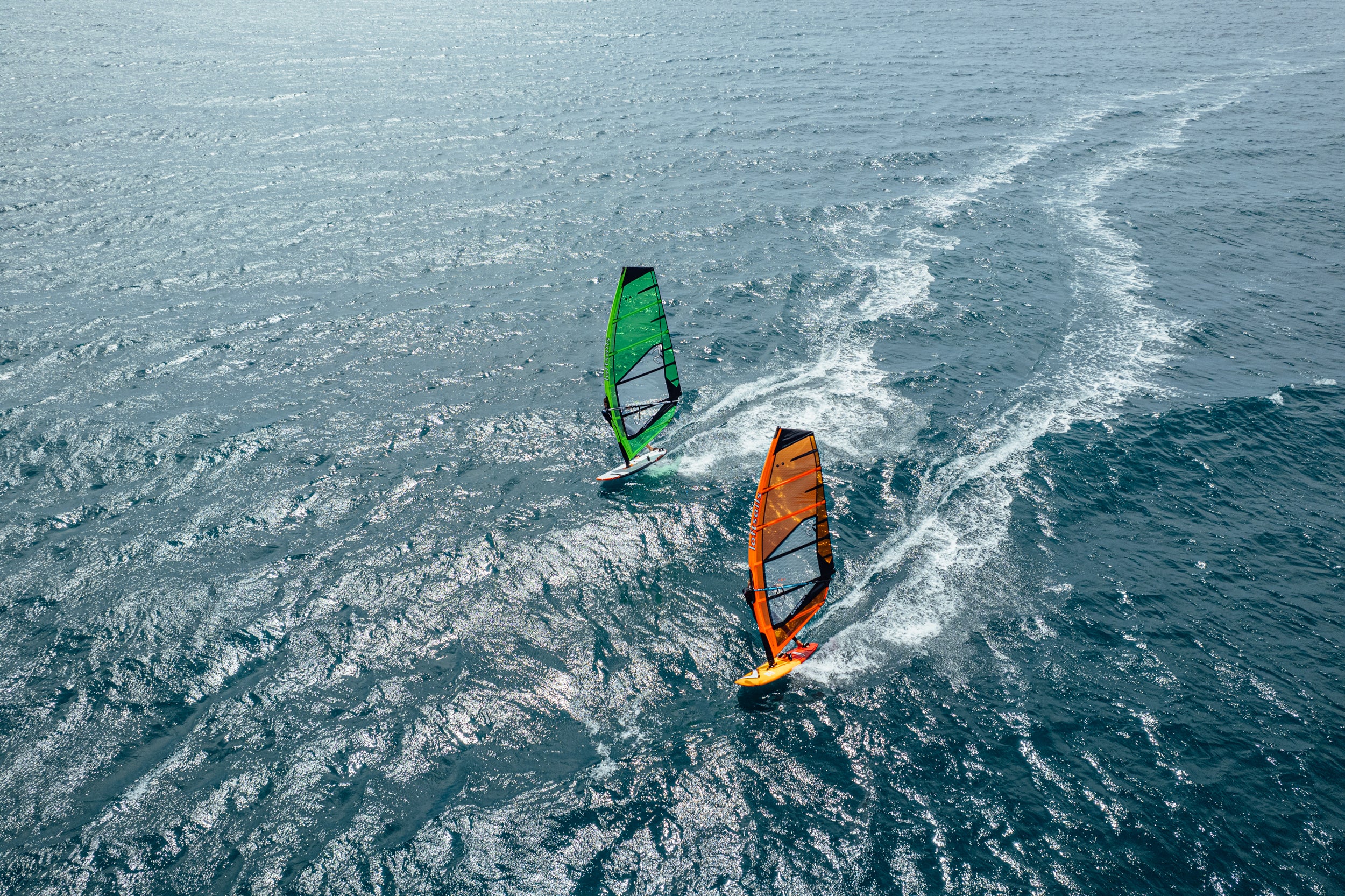Two windsurfers with colorful sails gliding over the ocean.