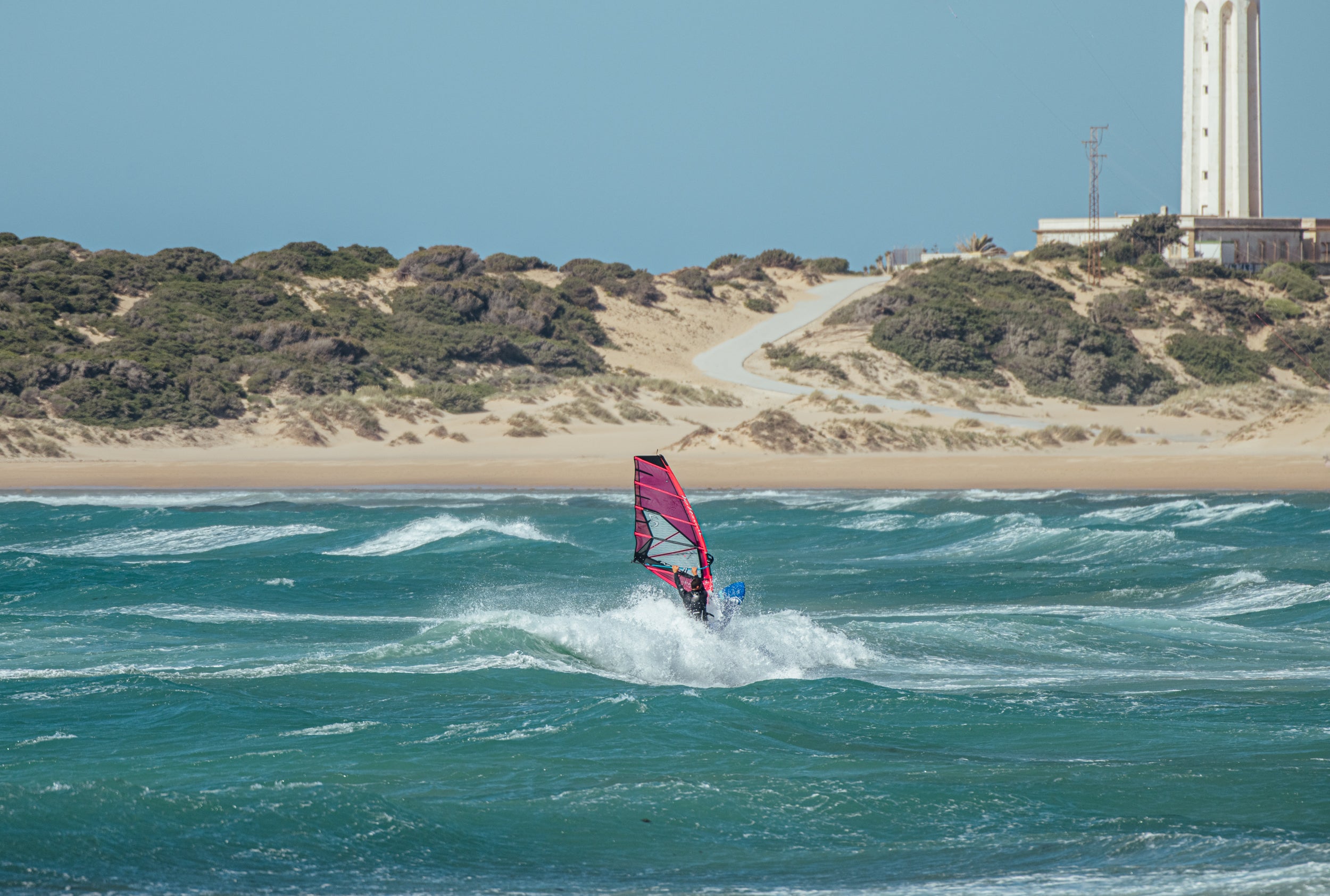 Person windsurfing in the ocean with a lighthouse in the background