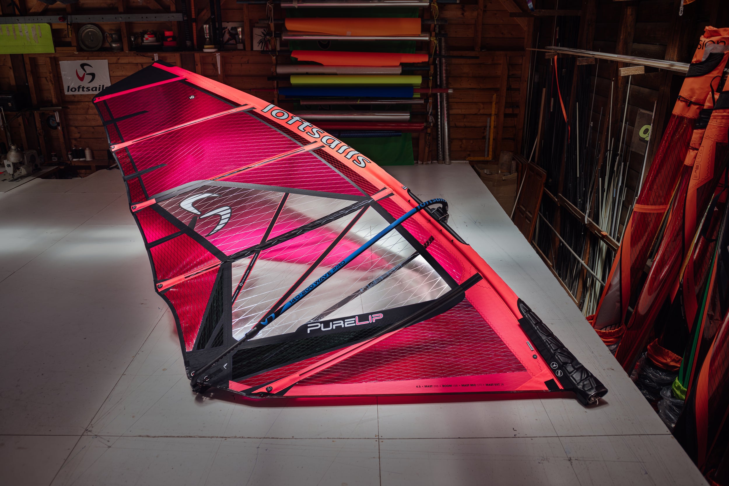 Red and black windsurf sail with 'Loftsails' branding on a table in a workshop setting