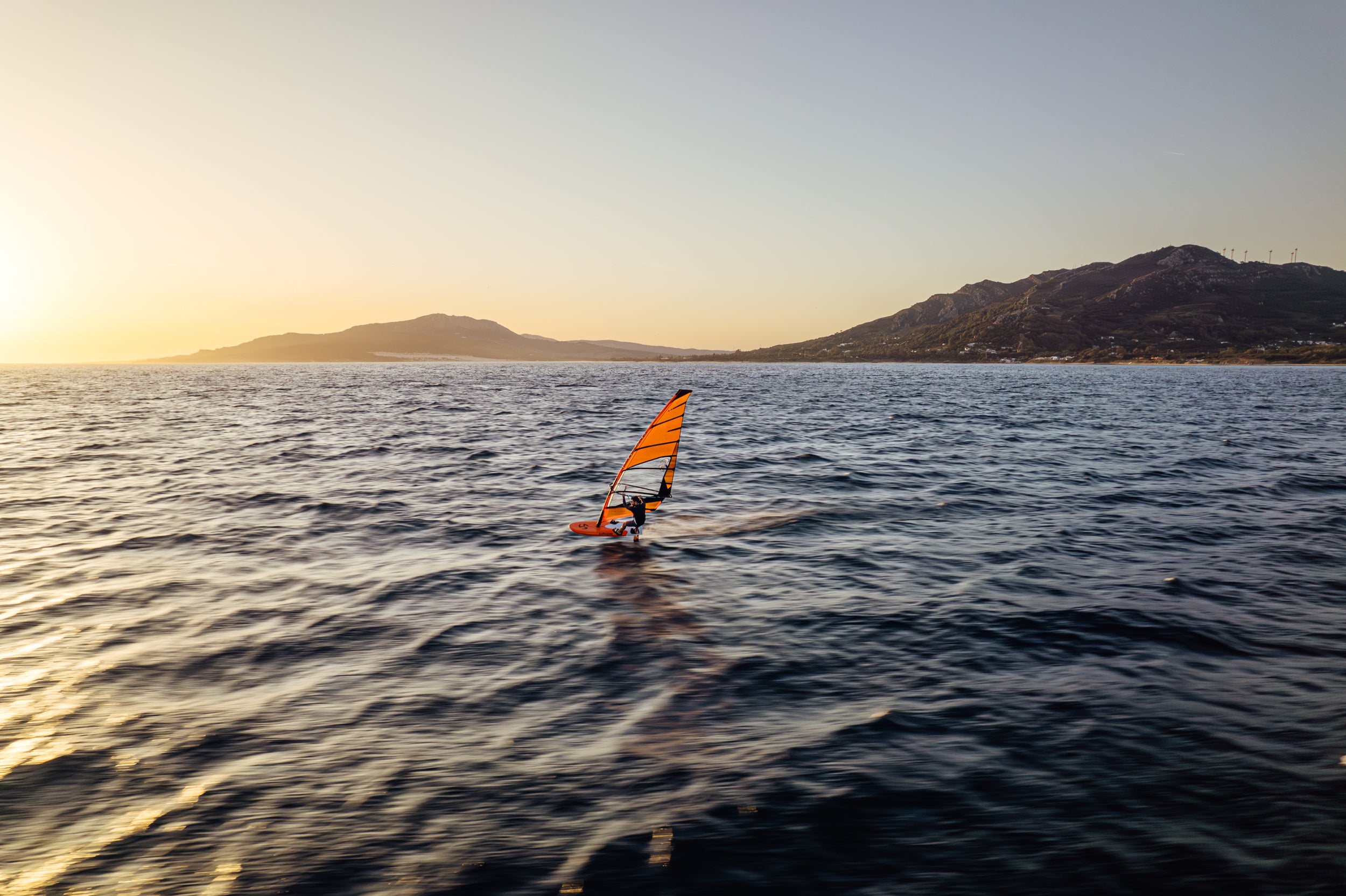 Person windsurfing on a body of water with mountains in the background during sunset.