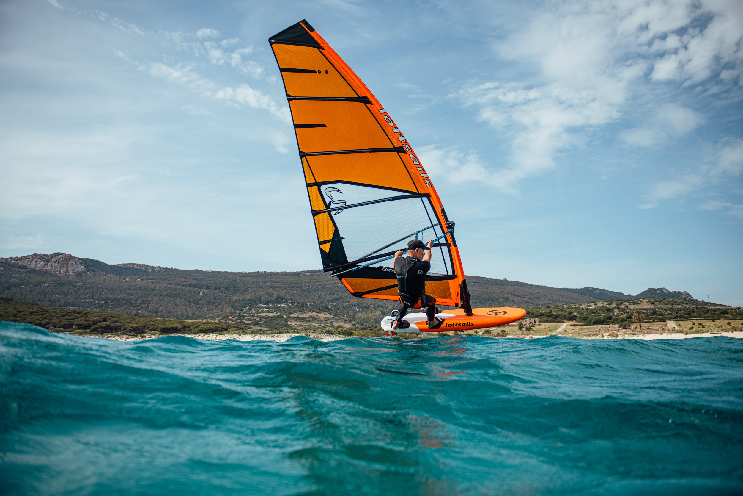 Person windsurfing on a blue ocean with mountains in the background