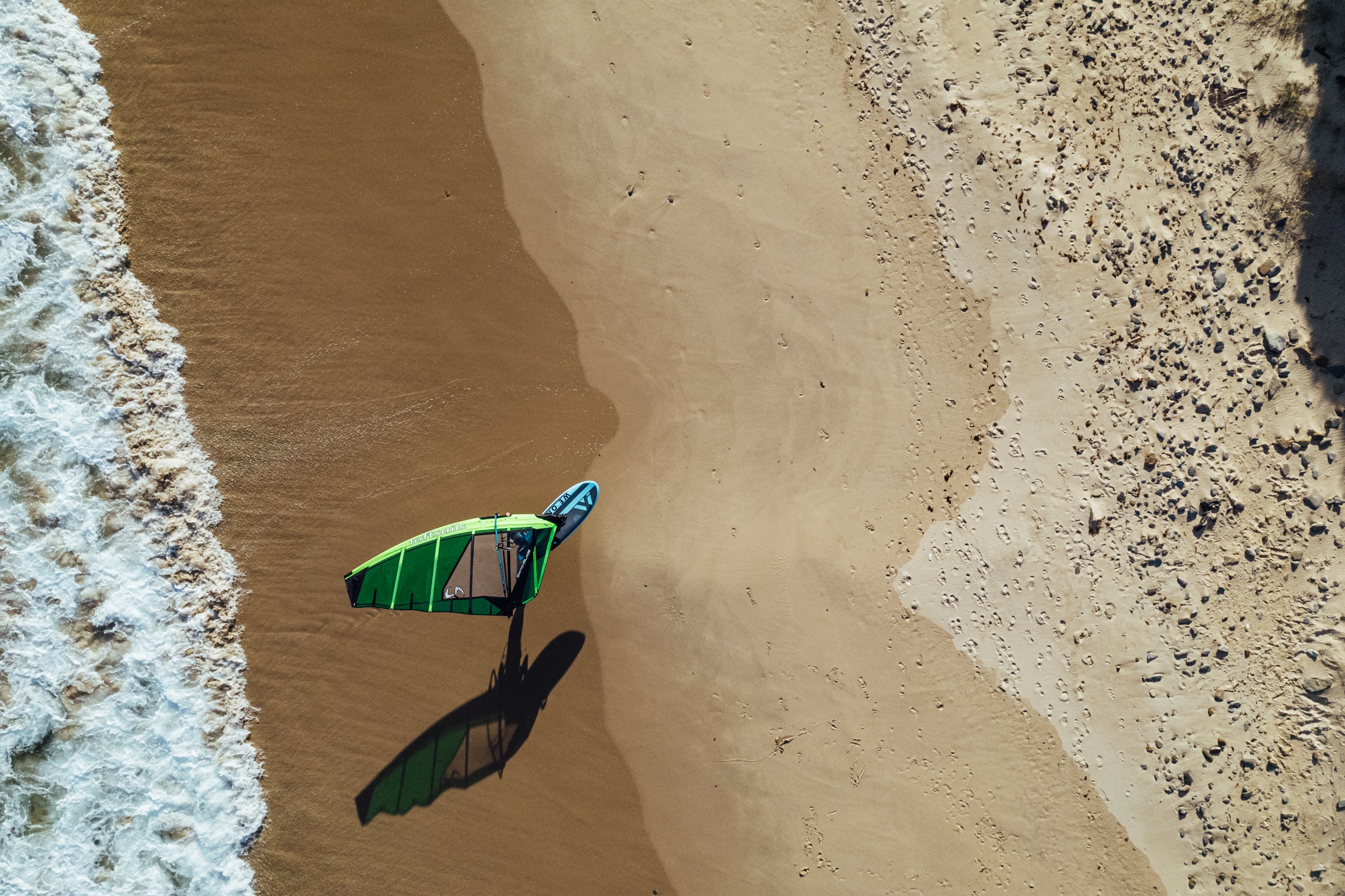 Green and blue windsurf board on a sandy beach with water at the edge.