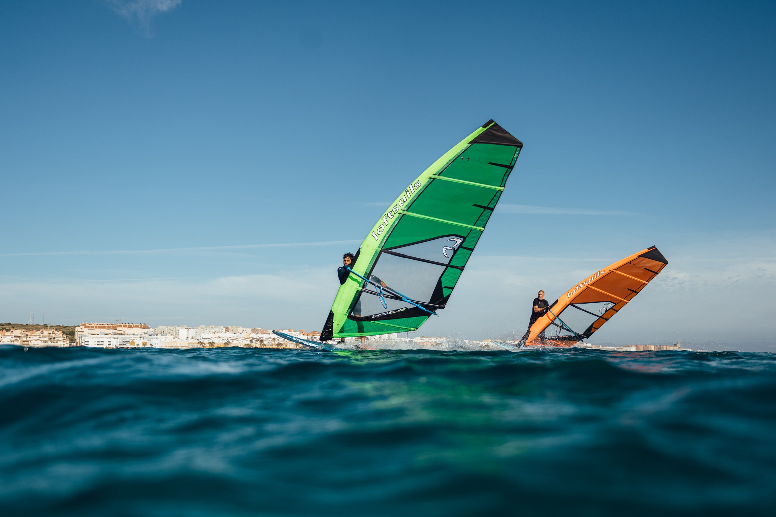 Two windsurfers on the water with a clear blue sky using a freeride sail from loftsails in tarifa