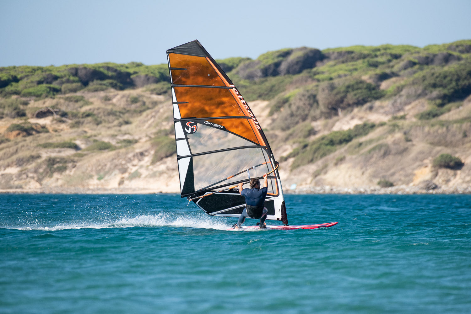 Person windsurfing on a blue body of water with a scenic background