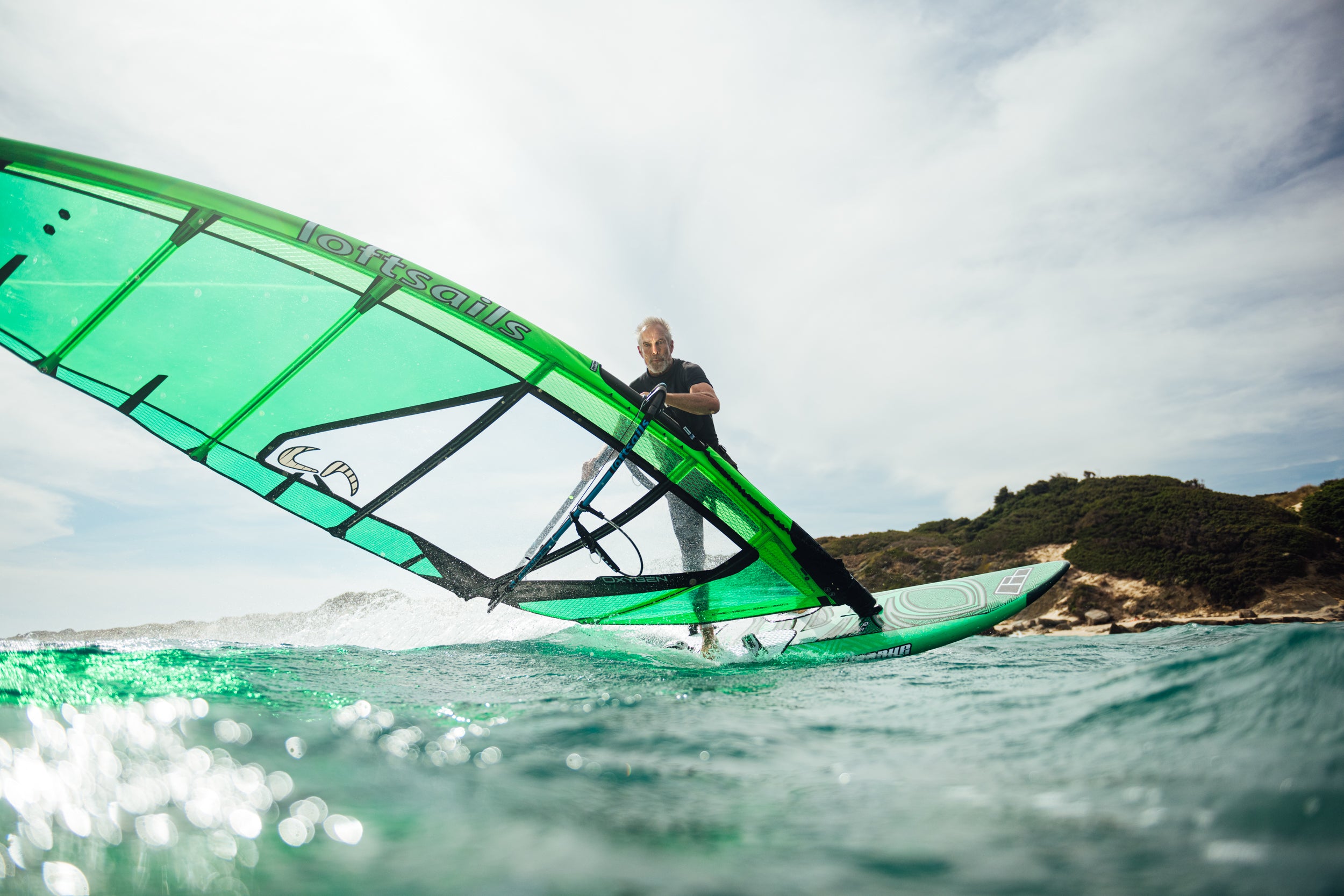 Person windsurfing on a green board with a sail in the ocean